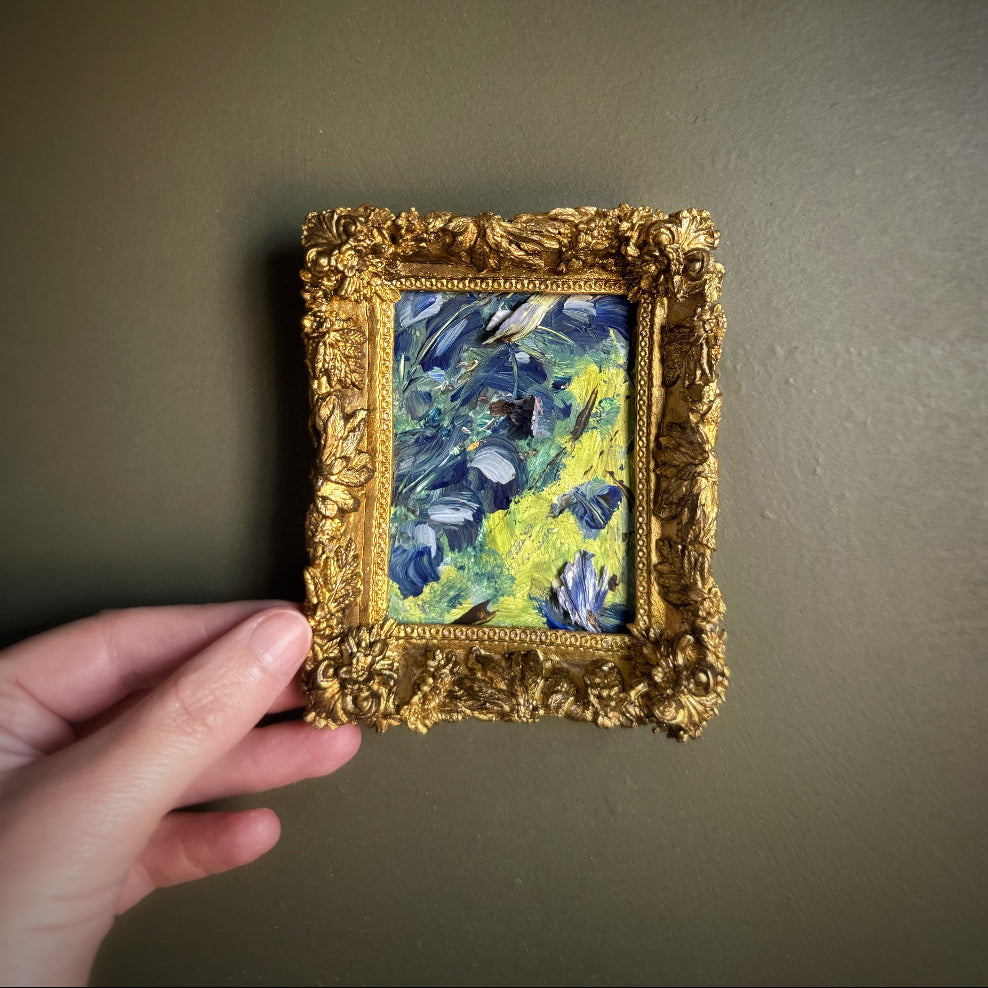 Miniature painting in a gold frame held by a hand against a plain background