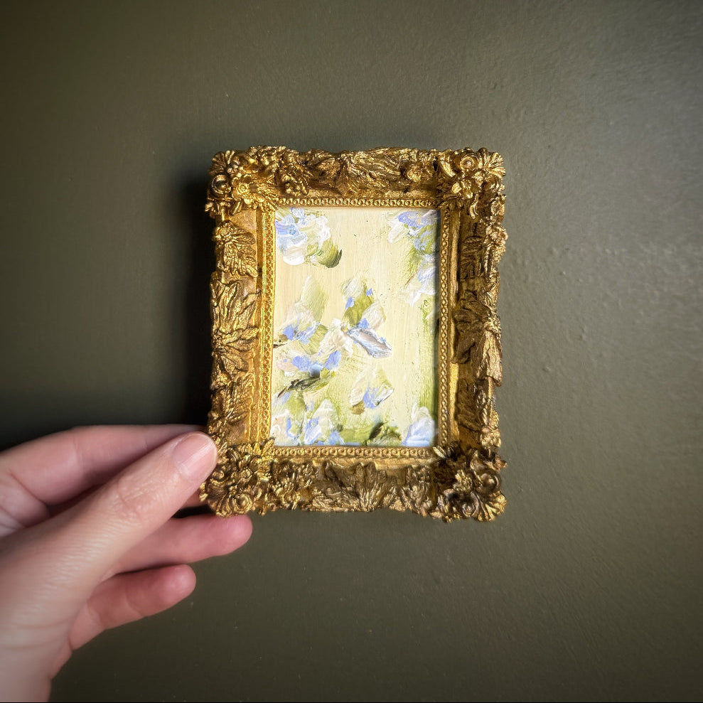 Gold-framed miniature painting held against a plain background