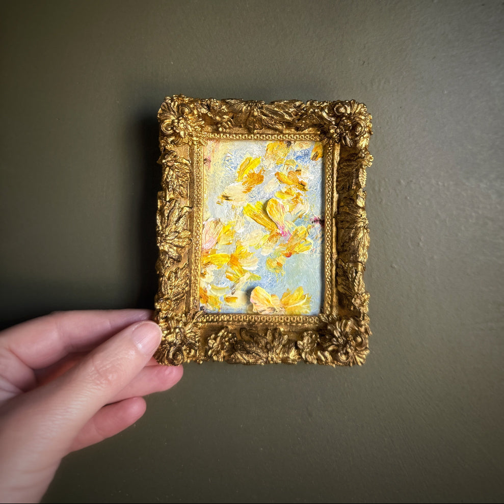 Small painting with a gold frame held by a hand against a dark background
