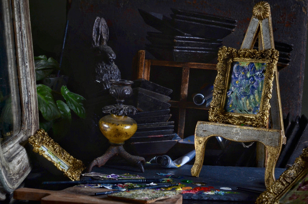 Artistic setup with easel, paintbrushes, and framed artwork in a dark room.