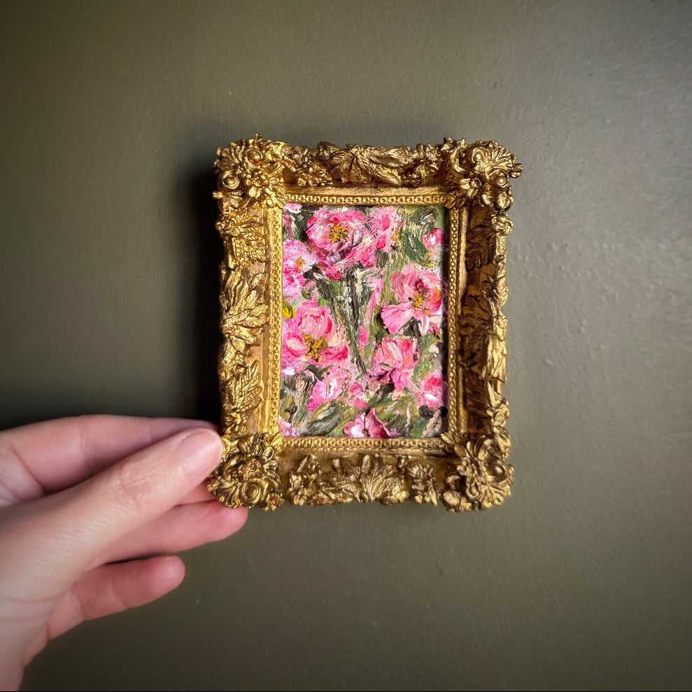 Gold-framed floral painting held against a plain wall