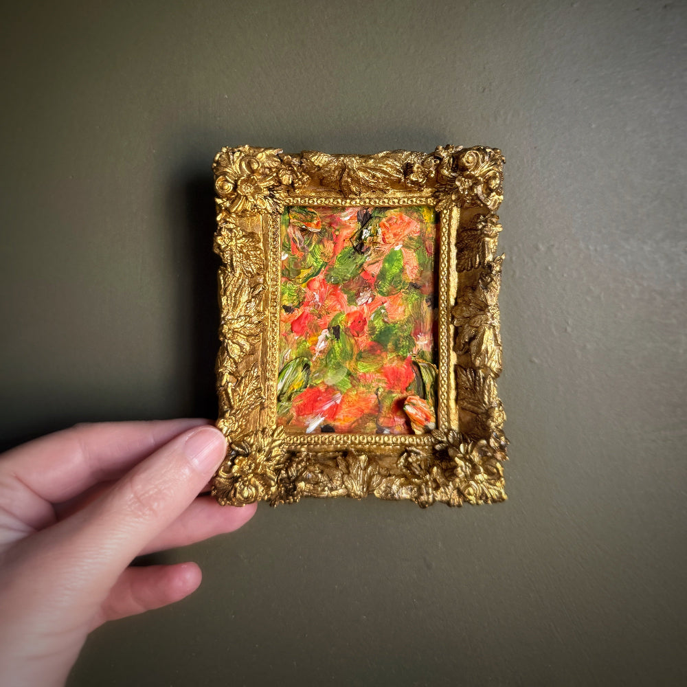 Hand holding a small gold-framed painting against a plain background
