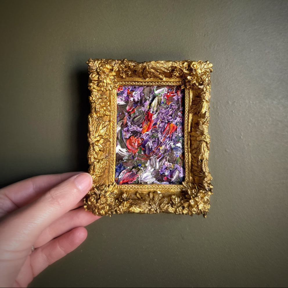 Gold-framed painting held by a hand against a dark background