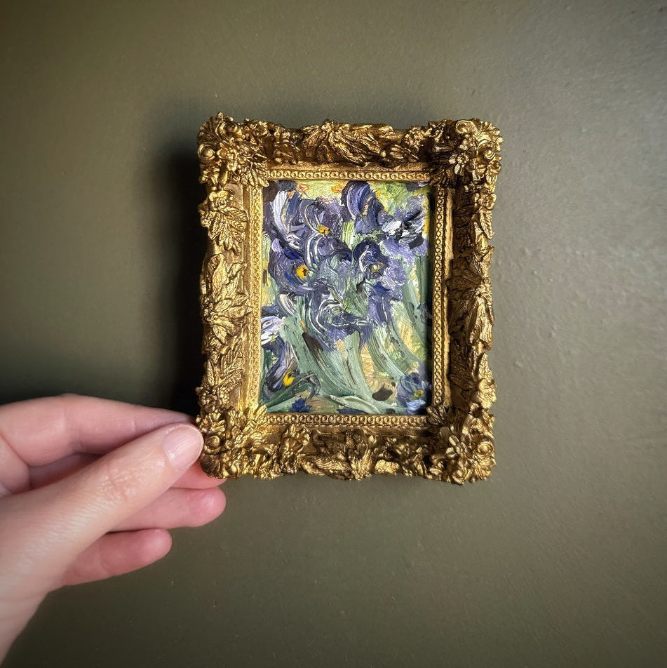 Miniature painting of Irises in a gold frame held by a hand against a plain background