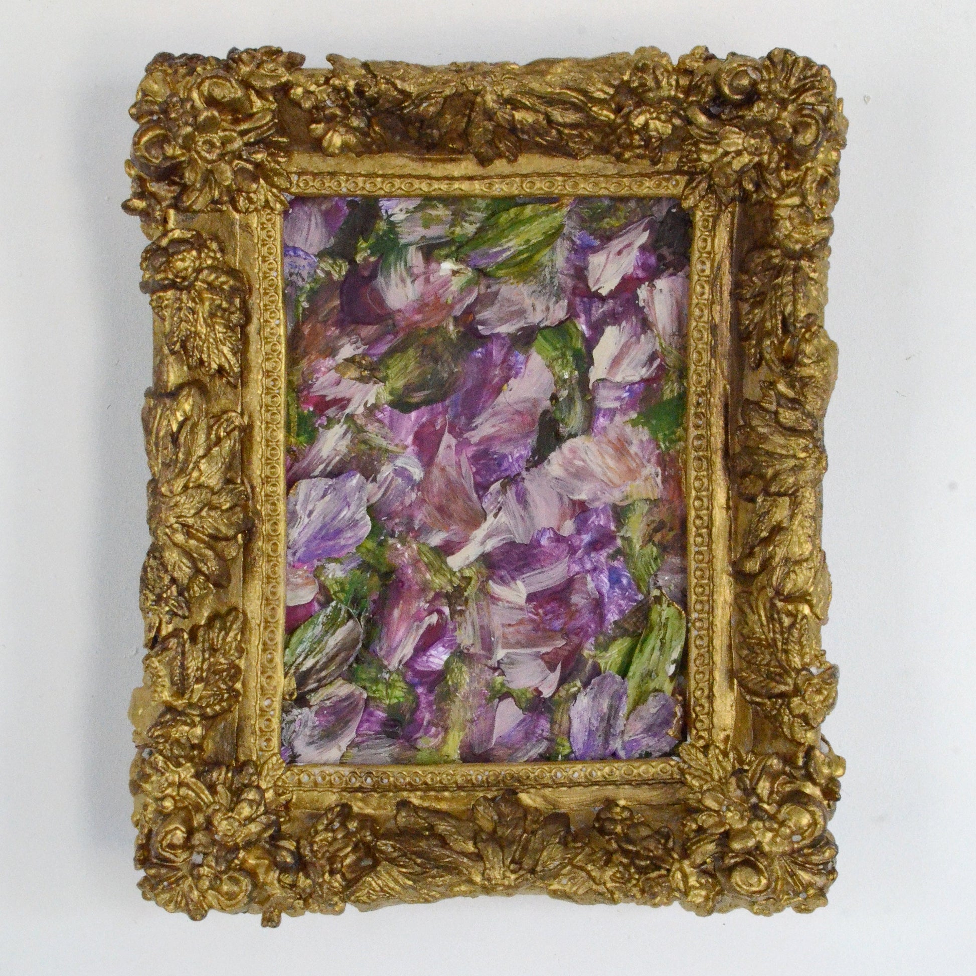Framed artwork of purple flowers with a gold frame on a white background