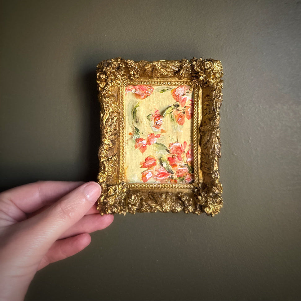 Small framed artwork with floral design held by a hand against a dark background