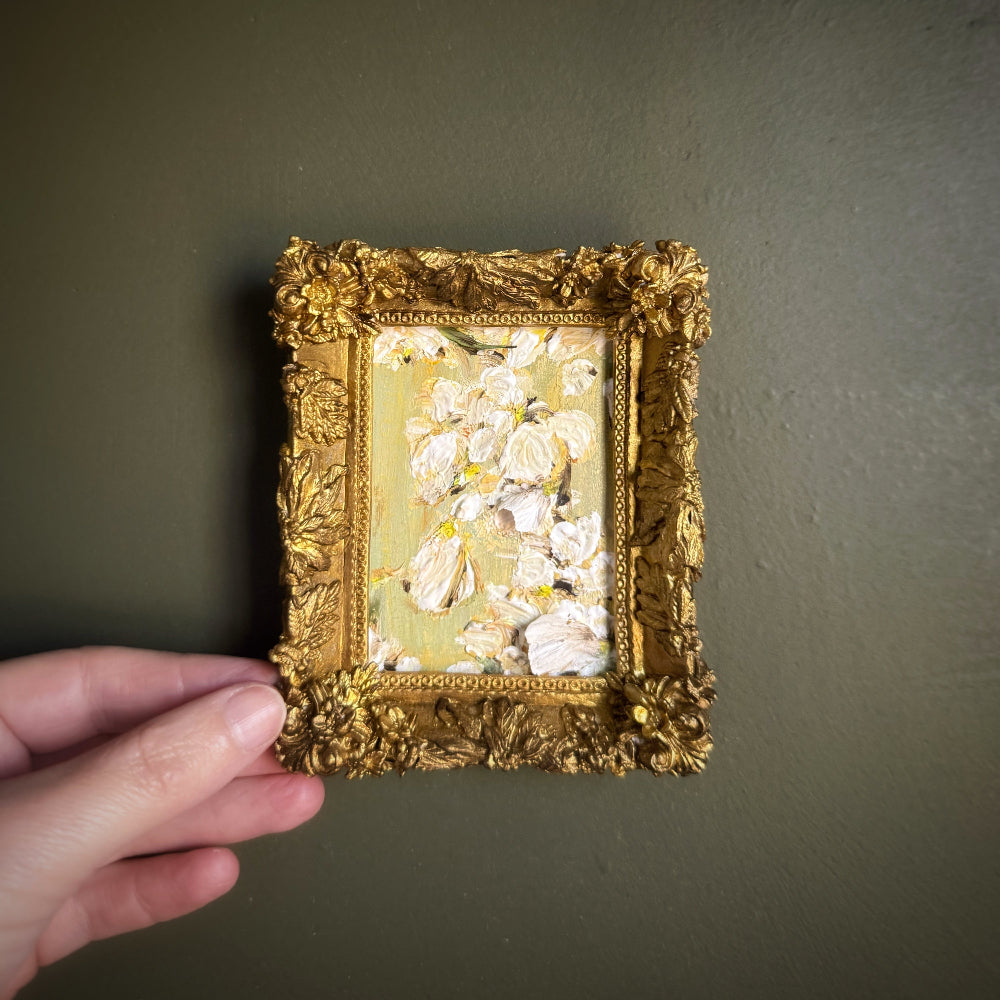 Decorative gold frame with floral design held against a dark green wall.