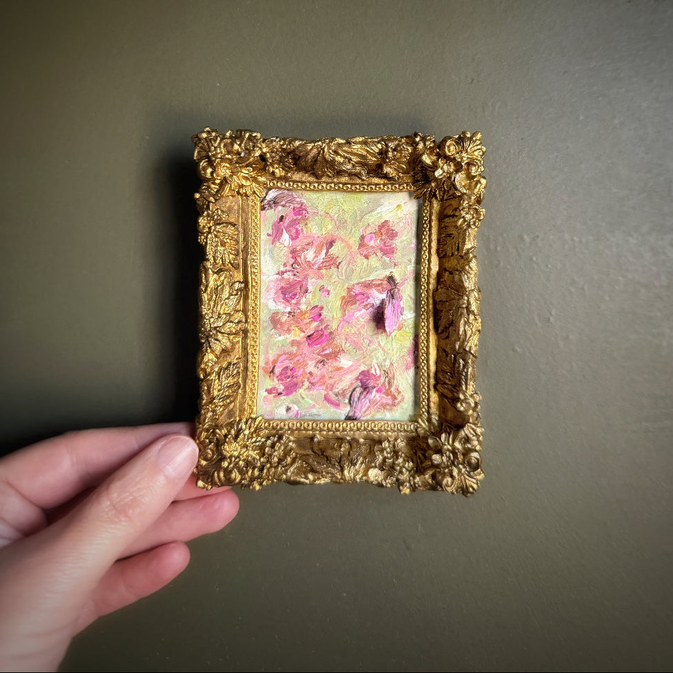 Small floral painting in a gold frame held against a dark background