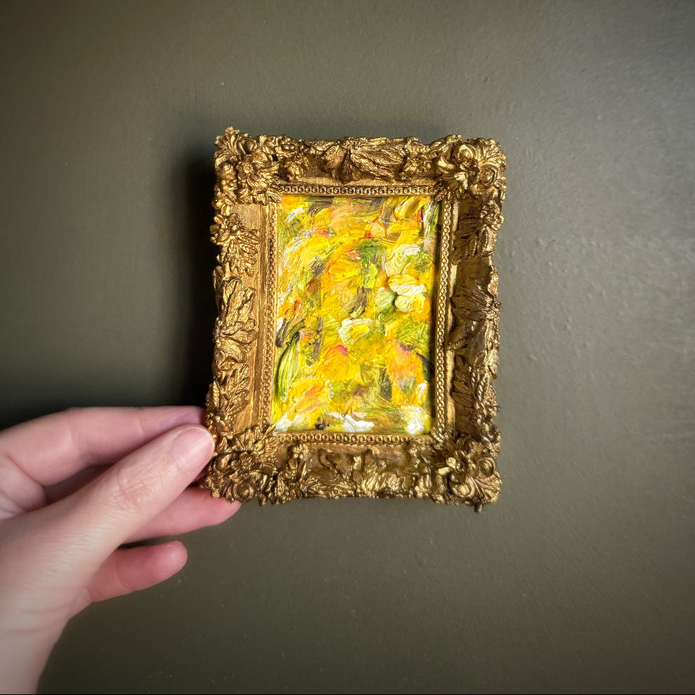 Hand holding a small gold-framed painting against a dark background