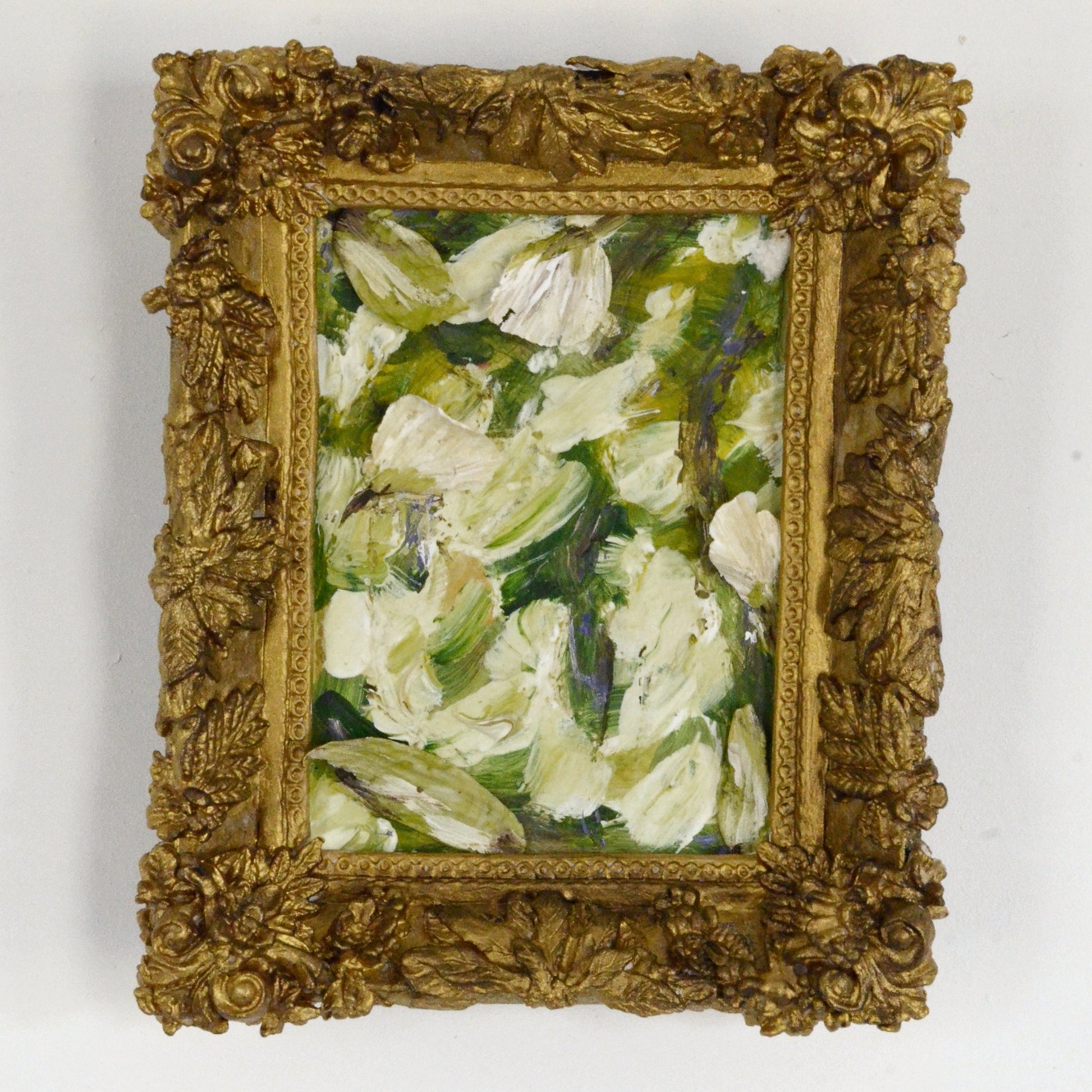 Small oil painting of flowers in a decorative gold frame on a white background