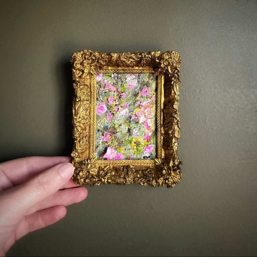 Gold-framed artwork with floral design held against a dark green wall